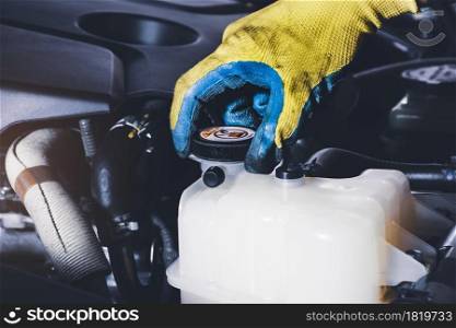 The mechanic hand is open or close the cap of coolant reservoir tank of car radiator to check the fluid level