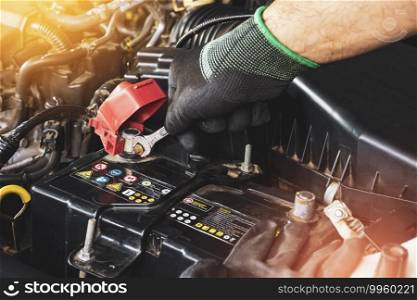The Mechanic hand wearing black gloves is fasten the bolt with the open-end wrench to replacement of the car old battery
