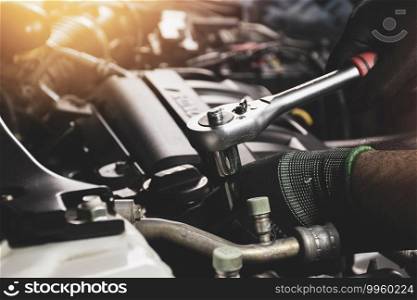 The Mechanic hand wearing black gloves is fasten the bolt with the socket wrench to repairing of the car engine
