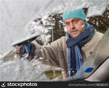 The mid adult man cleans a frozen windshield