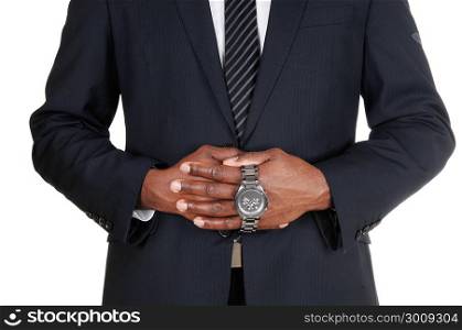 The middle section of an African man in a dark suit holding his wristwatch with both hands, isolated for white background