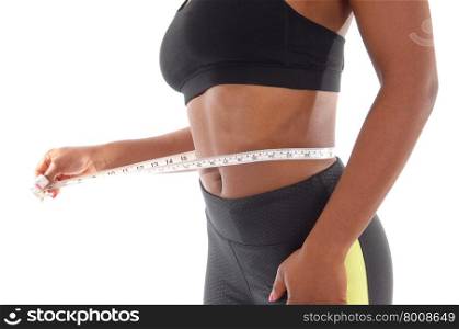 The midsection of a African American woman measuring her waist in a black sports bra and pants, isolated for white background.