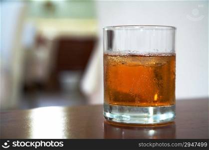 The misted over glass of whisky with an ice on a table