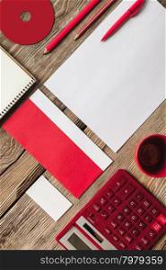 The mockup on wooden background with red calculator, pen, pencil, cup of coffee, white blank paper for writing, notebook and disk