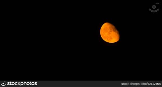 The moon takes on an orange hue in a dark night