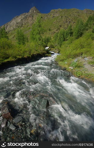 The mountain river in the mountains. Current through the gorge the river. Stones and rocky land near the river. Beautiful mountain landscape. The mountain river in the mountains. Current through the gorge the river. Stones and rocky land near the river. Beautiful mountain landscape.