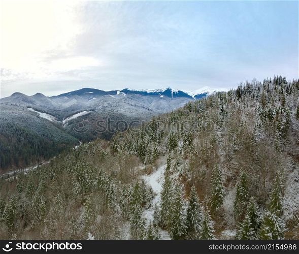 The mountains are covered with forest. The first snow on the ground and branches. Overcast. Aerial view. Beginning of Winter in the Mountains. Aerial View