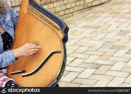 The musician plays the old Ukrainian ethnic musical instrument bandura (pandora) against the background of the old cobblestone road.. Old ukrainian ethnic musical instrument bandura (pandora) close up.