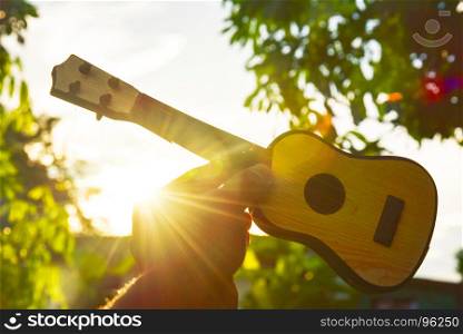 The musicians holding guitar in the sky at sunset. Success concept