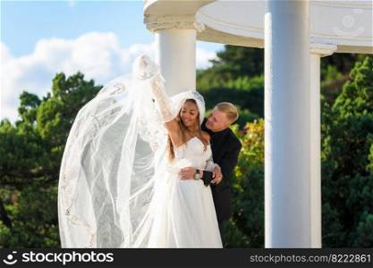 The newlyweds happily embrace in a beautiful gazebo against the backdrop of foliage and sky