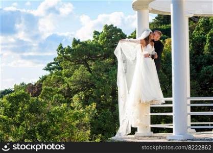 The newlyweds happily embrace in a beautiful gazebo with columns against the backdrop of foliage and sky