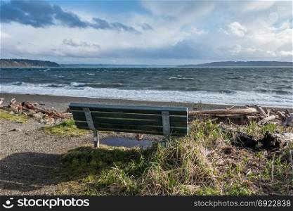 The normally placid Puget Sound is filled with whitewater on a windy day. Bench in the foreground.