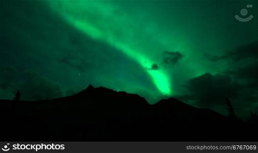 The Northern Lights emerge through the clouds in remote Alaska