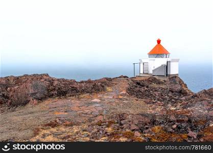 The norway sea beacon with a red top and a stone footpath on the edge of the rock over the foggy sea. The sea beacon with a red top and a stone footpath on the edge of the rock over the foggy sea