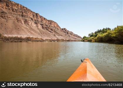 The nose of a kayak is in the foreground as people kayak along the Orange River on the border of South Africa and Namibia.