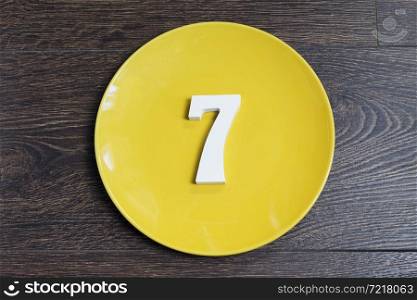 The number seven on a yellow plate and brown background.. The number seven on a yellow plate.