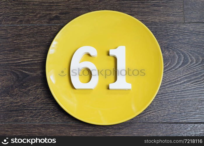 The number sixty-one on the yellow plate and brown background.. The number sixty-one on the yellow plate.