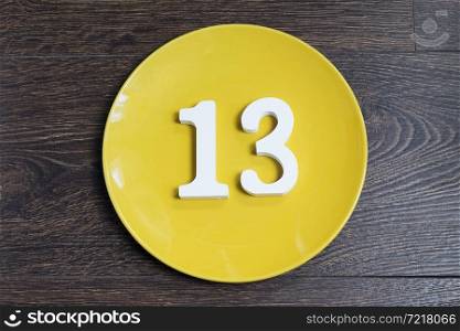 The number thirteen on the yellow plate and brown background.. The number thirteen on the yellow plate.