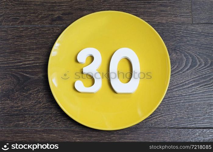 The number thirty on yellow plate and brown background.. Figure thirty on the yellow plate.
