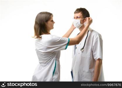 The nurse puts a medical mask on the doctor’s face with glasses