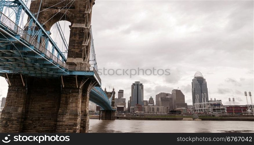 The Ohio River is at flood stage as it passes underneath a historical suspension bridge
