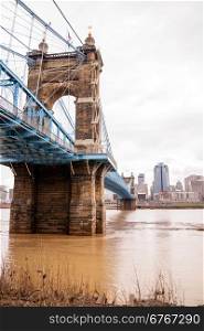 The Ohio River is at flood stage as it passes underneath a historical suspension bridge