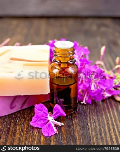 The oil in a dark bottle and two bars of homemade soap with fireweed flowers on the background of wooden boards