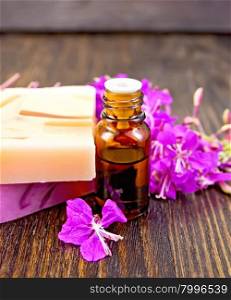The oil in a dark bottle and two bars of homemade soap with fireweed flowers on the background of wooden boards