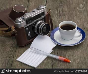 the old camera, coffee and notebook with the handle on a wooden table, a festive card a retro subject