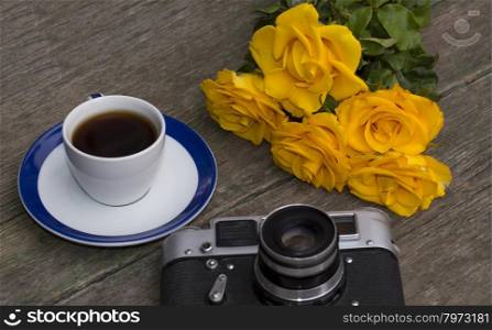 the old film camera, roses and coffee on a wooden table