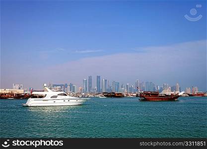 The old harbour in Doha, Qatar, with dhows and a luxury yacht. The high-rise skyline of the new business district is in the background. Shot in January 2011.