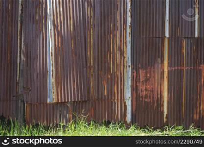 The old weathered and distressed rusty corrugated zinc wall with green grass