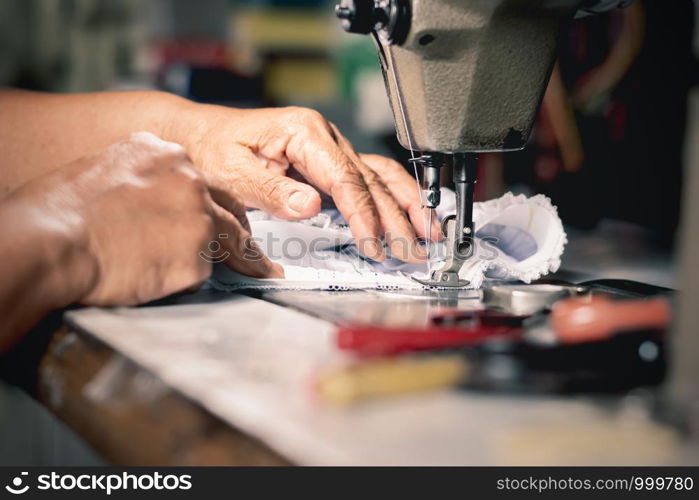 The old woman's hand is using a sewing machine.