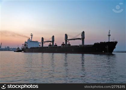 The ore carrier heaves out of the harbor on a tow, the photo is taken at sunset.
