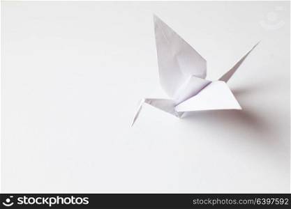 The origami crane is made of white paper, isolated on a white background. White crane handmade