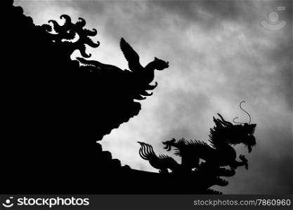 The outline of a phoenix chasing a dragon on the rooftop of the Mengjia Longshan Temple in Taipei. The atmosphere is accentuated with a silhouette of the creatures against a moody sky.