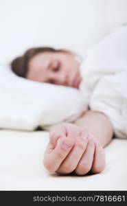 The outstretched hand of a sleeping woman lies on the mattress, the face of the brunette woman out of focus in the background