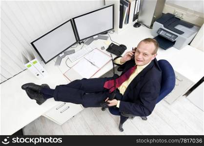 The owner of a small business relaxing behind his desk making several phone calls