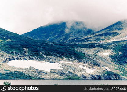 The peak view from the shore of a mountain lake. Journey through the hill country. Tourist attractions, natural beauty.