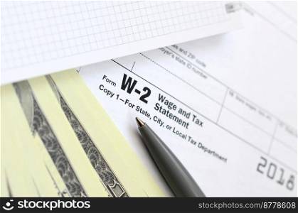 The pen, notebook and dollar bills is lies on the tax form W-2 Wage and Tax Statement. The time to pay taxes