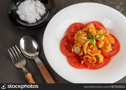 The pipe rigate italian pasta with tomato sauce and egg, chili and fresh tomato slice in white plate, salt in black bowl with fork and spoon, copy space and selective focus