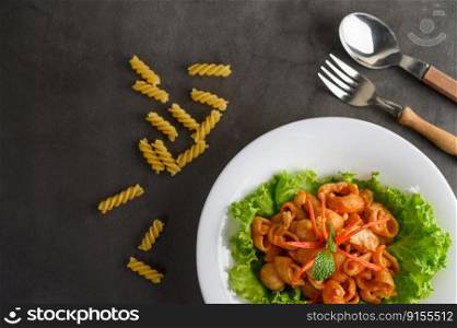 The pipe rigate italian pasta with tomato sauce and egg, chili and fresh tomato slice in white plate with fork and spoon, copy space 