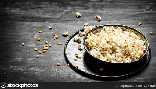 The popcorn in the plate. On the black wooden table.. The popcorn in the plate.