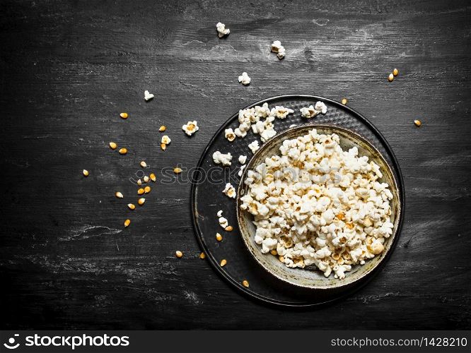 The popcorn in the plate. On the black wooden table.. The popcorn in the plate.