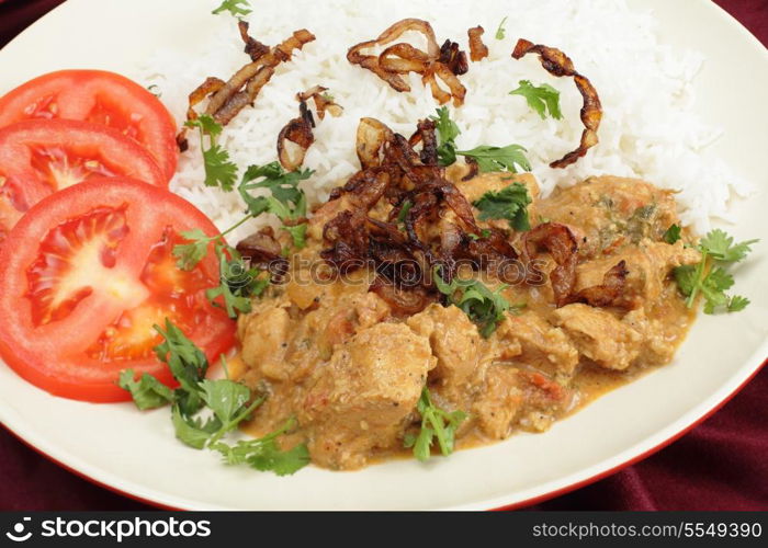The popular south-Indian variant of Chicken Korma, incoporating coconut, seen closeup, served with boiled basmati rice and garnished with coriander leaves, fried onion and sliced tomato.