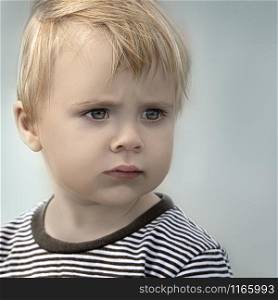 the portrait of thinking small blond boy at blue background