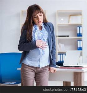 The pregnant woman struggling to do work in office. Pregnant woman struggling to do work in office