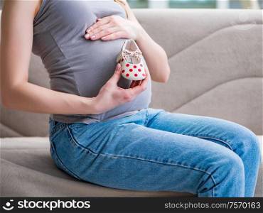 The pregnant woman with a belly tummy sitting on a sofa at home. Pregnant woman with a belly tummy sitting on a sofa at home