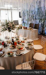 The presidium of the newlyweds in the banquet hall of the restaurant is decorated with candles and green plants, wisteria hangs from the ceiling