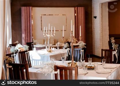 the presidium of the newlyweds in the banquet hall of the restaurant is decorated with candles and green plants, the general tone of the hall is beige